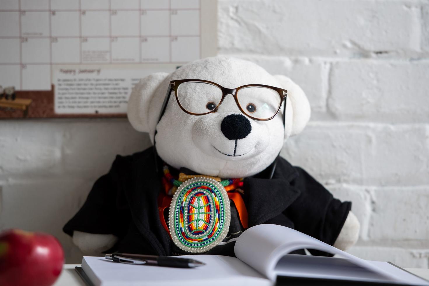 white stuffed bear wearing glasses reading a book