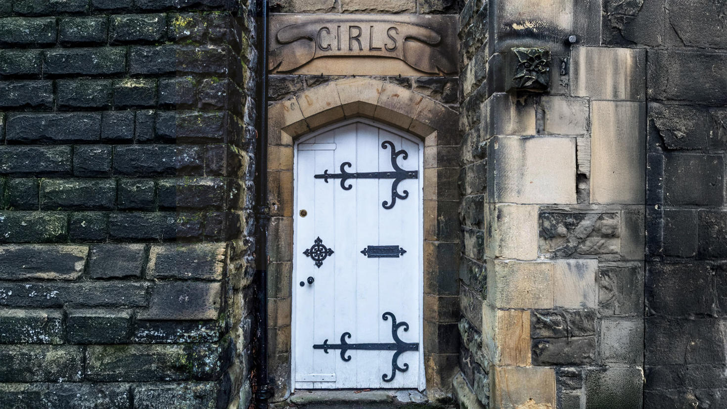 The word 'Girls' engraved above an old door at the entrance to stone building.