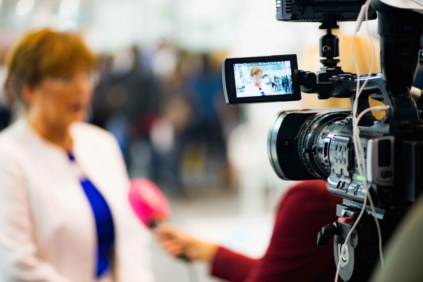 person being interviewed by journalist out of focus with news camera in focus