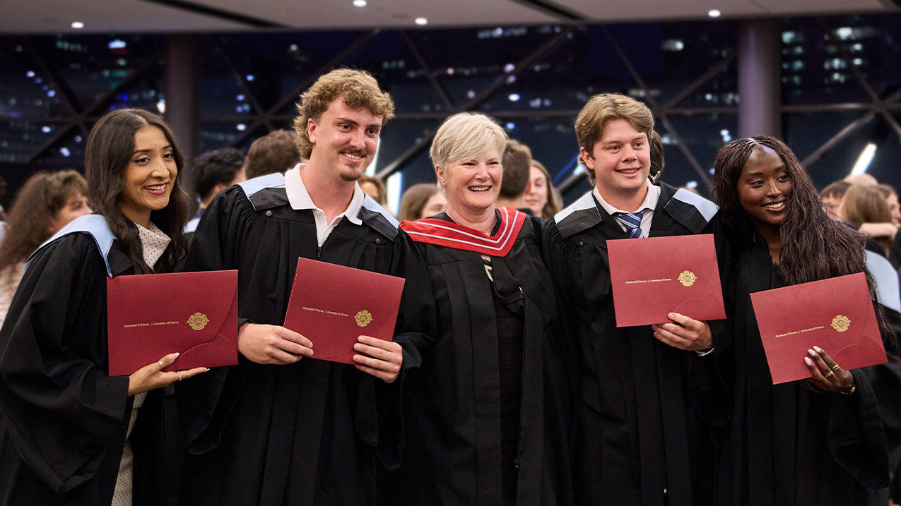Students holding diplomas standing with a professor