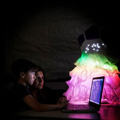 Student and teacher working on computer with rainbow coloured glow-up dress in the background.