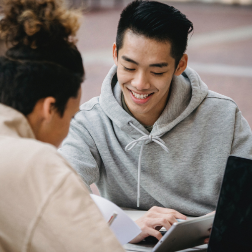 2 students sitting across from one another looking at a tablet.