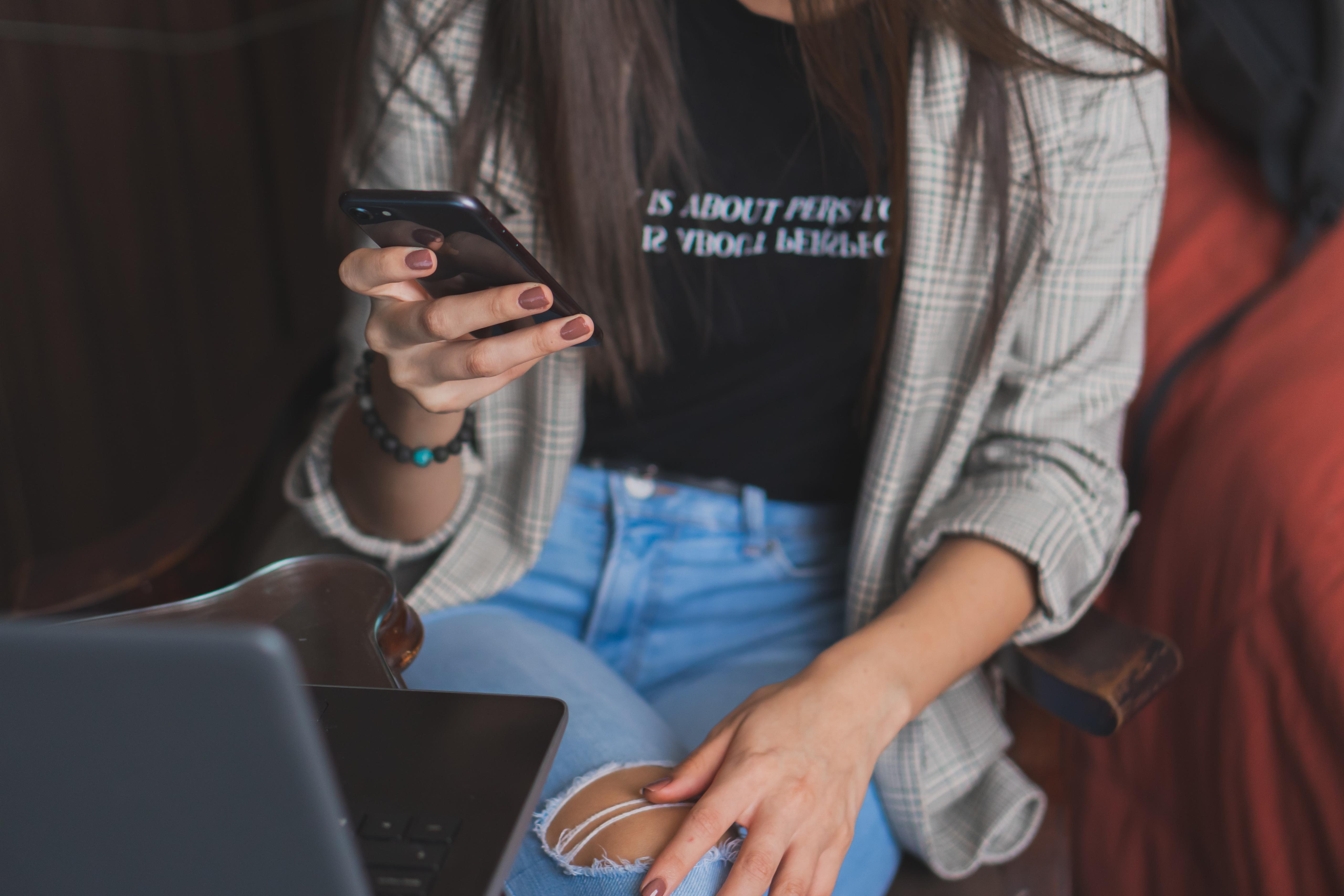A person looking at her phone with a computer in front of them.