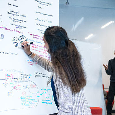 Student writing on whiteboard in the Simon Nehme Design Commons.