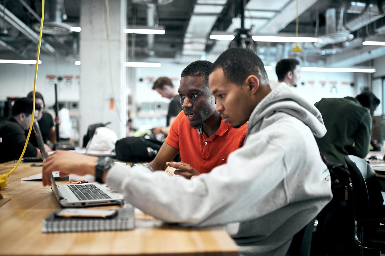 Two students working at a laptop in an engineering space.
