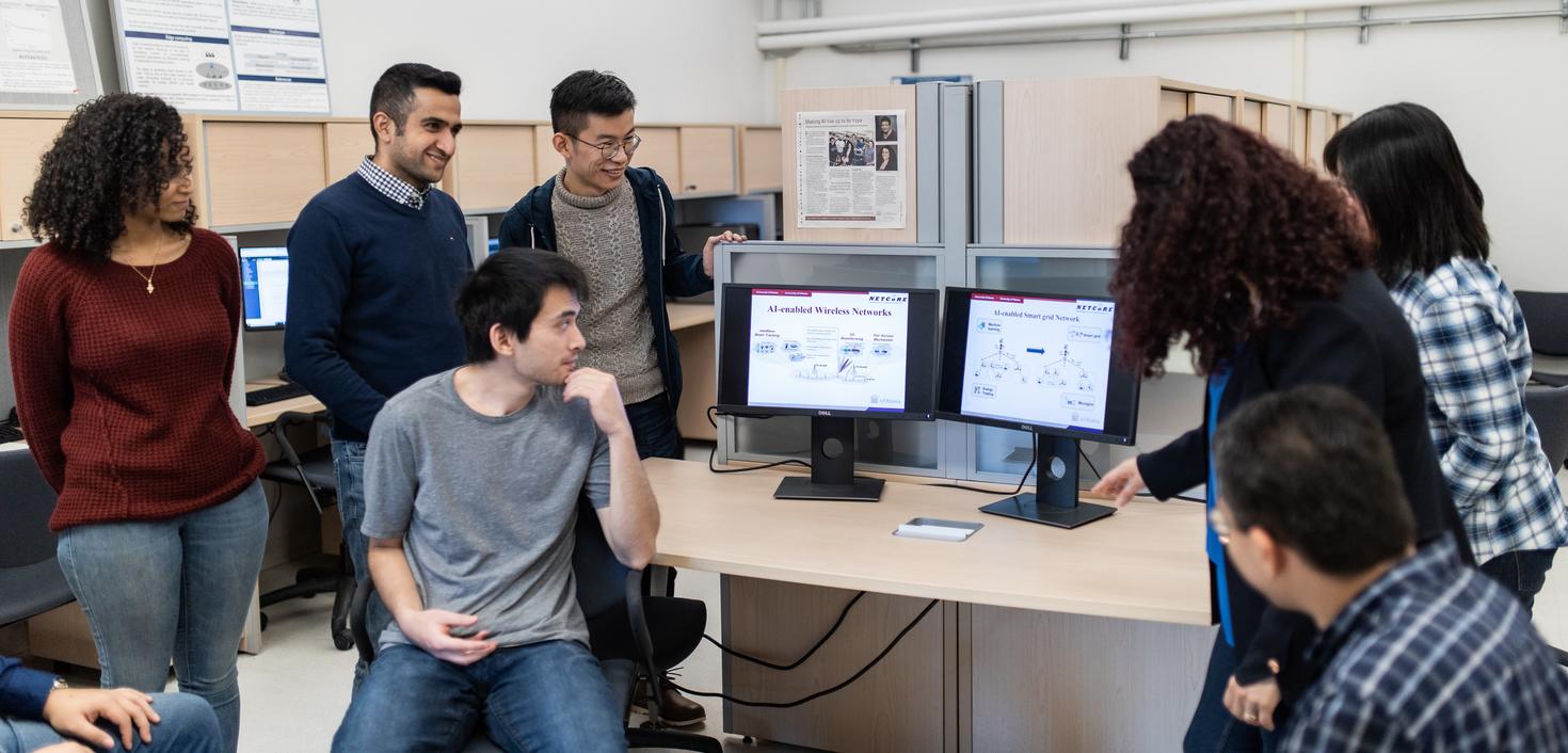 Group of engineering students and professor in conversation around data shown on a screen.