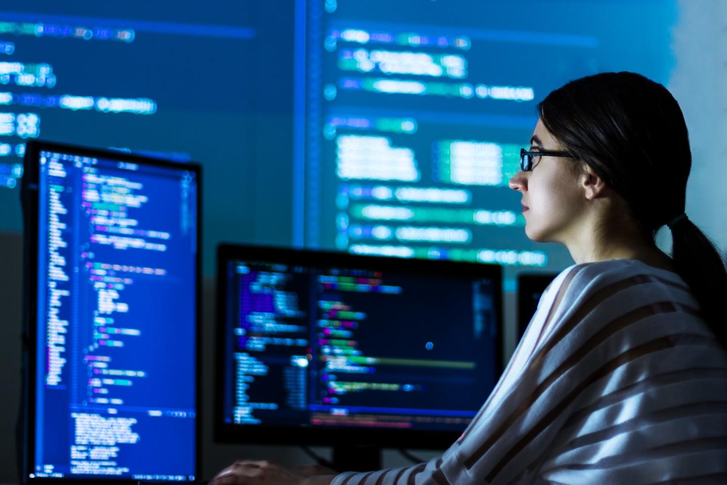 A person looks at code on multiple computer screens.