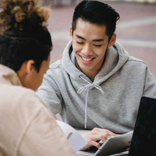Two students sitting across from one another looking at a tablet.