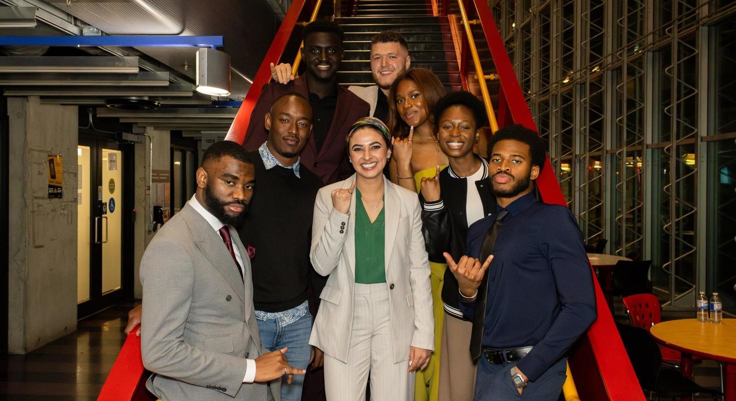 Group of people standing on a staircase, holding up up their pinkies with their iron rings.