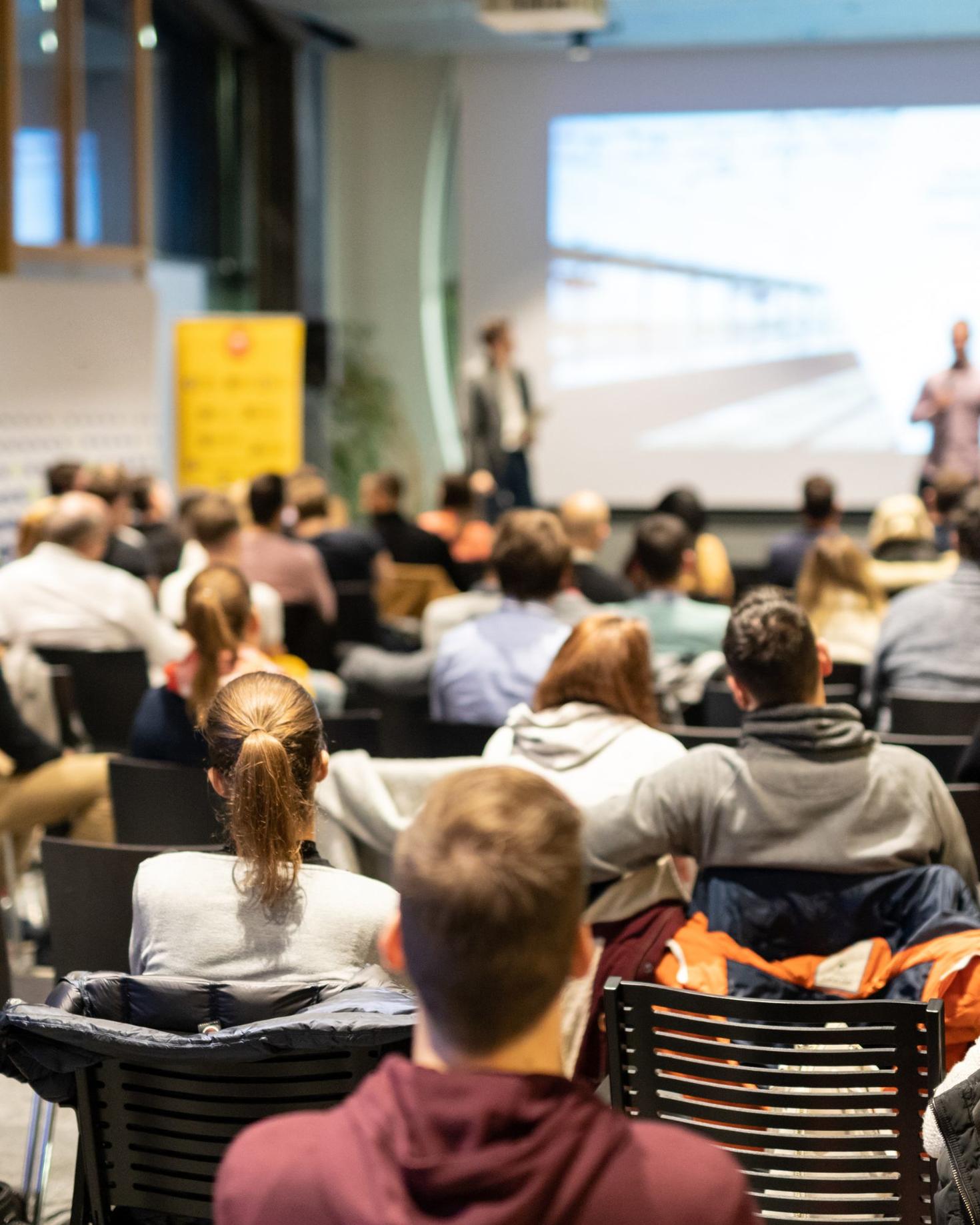 Crowd listening to a group presenting on a stage.