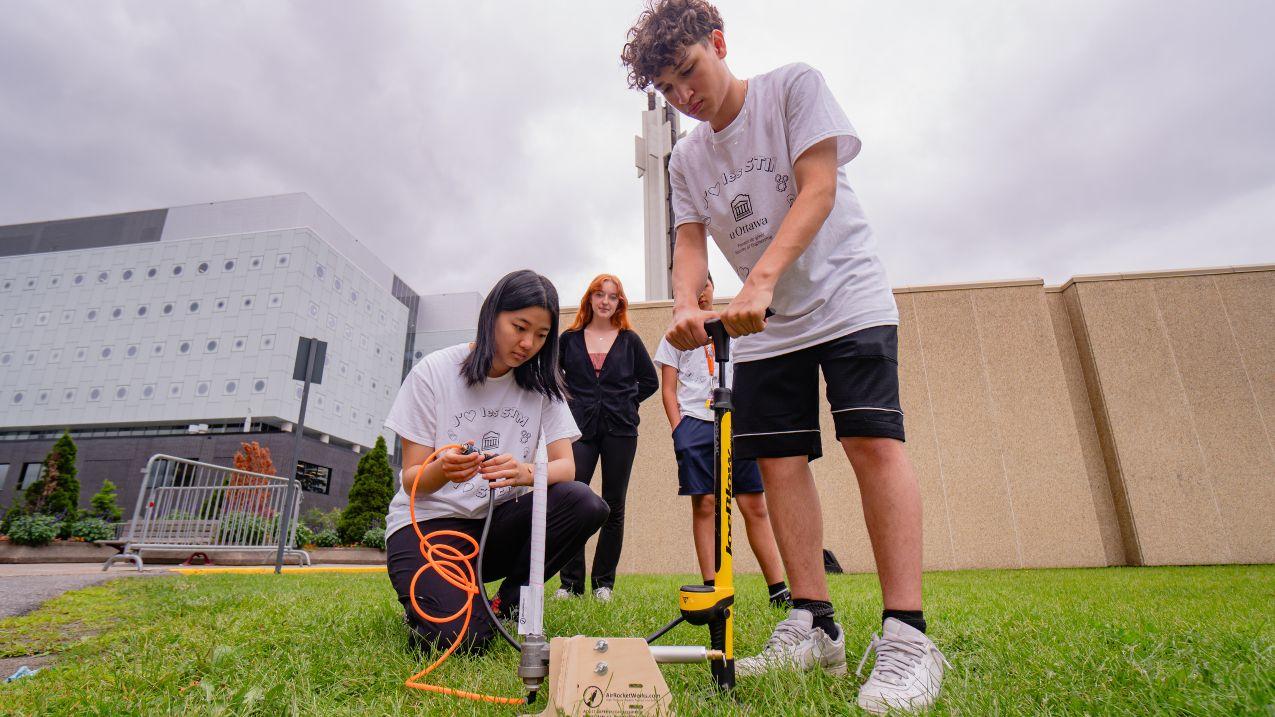 4 students on the grass working on a rocket. 