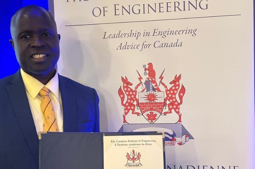 Mamadou Fall holding up his award in front of a roll up banner for the Canadian Academy of Engineering.