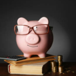 Piggy bank sitting on top of books, wearing glasses.