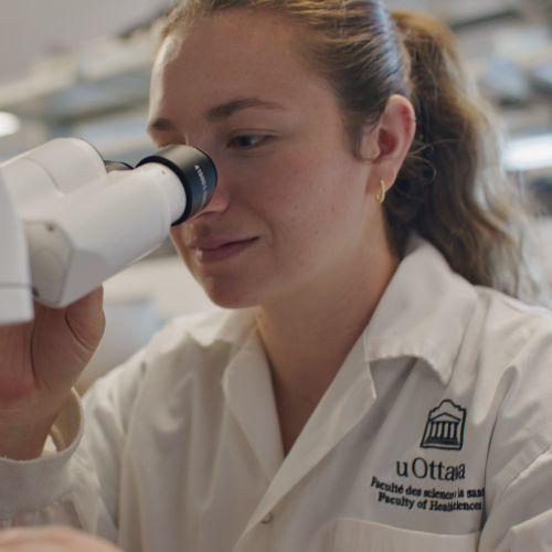 Photo of a blond girl looking into a microscope