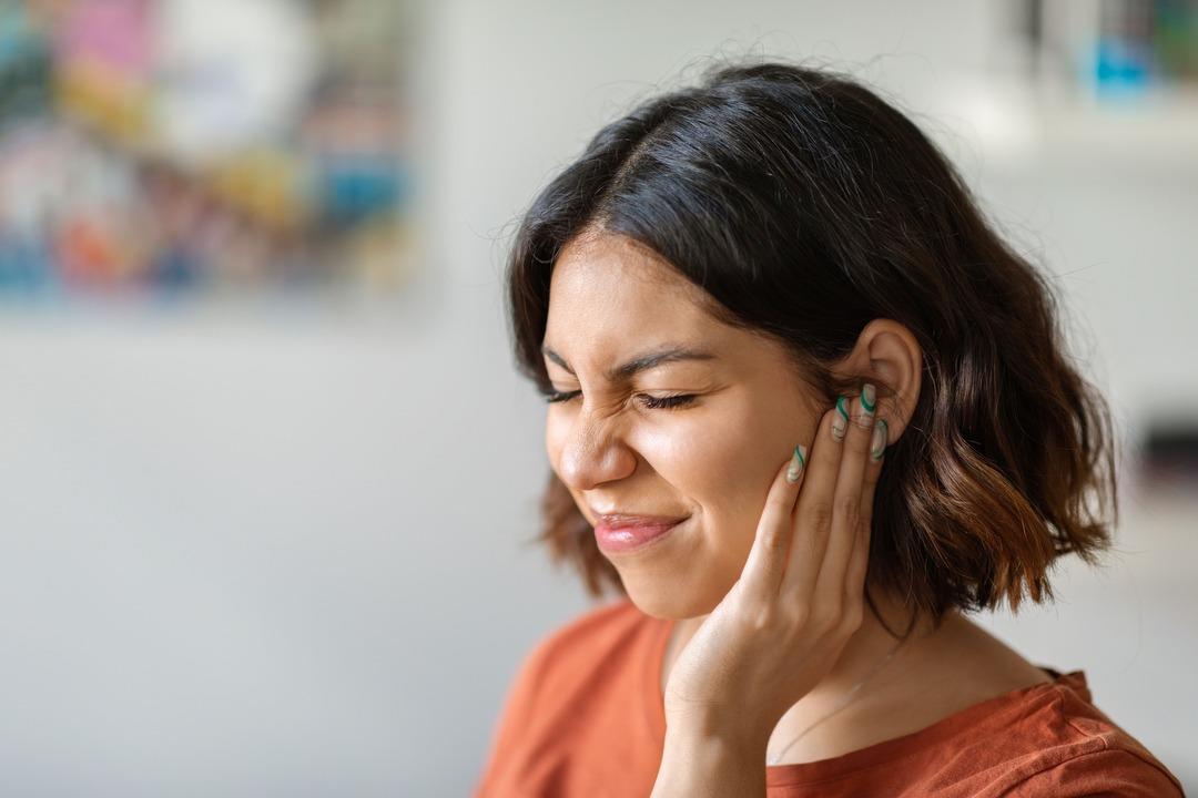 Woman holding ears, experiencing tinnitus symptoms.