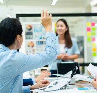 woman leading a whiteboard meeting with a man who has his hand up