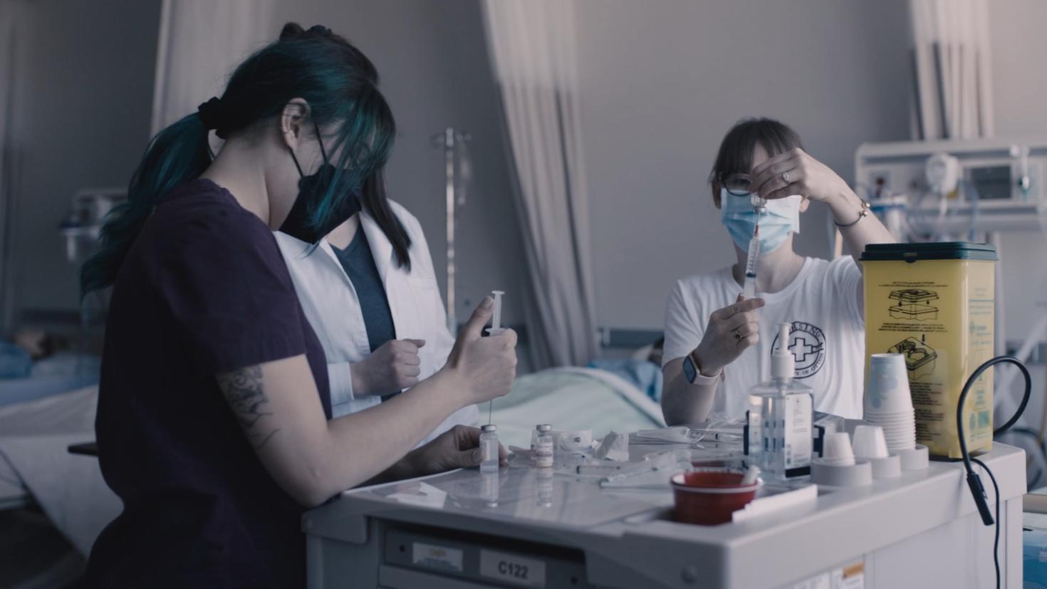 Nursing students, wearing masks, prepare injections in a simulated environment.