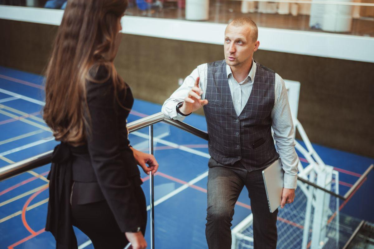 Woman and man talking on a stairway with a basketball court in the background
