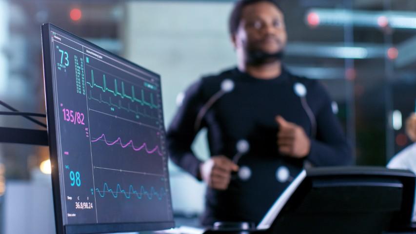 A screen reads out data as a man runs on a treadmill in the background