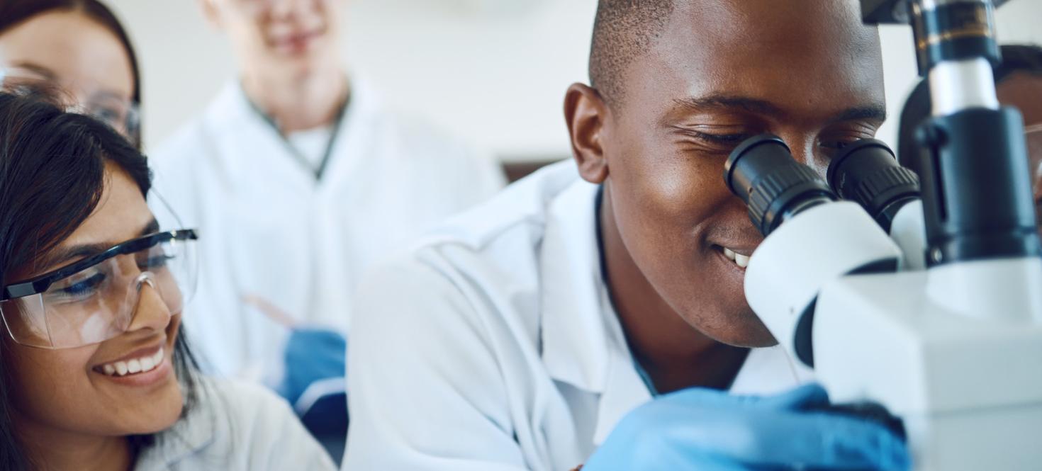 several people smiling as one man looks through a microscope