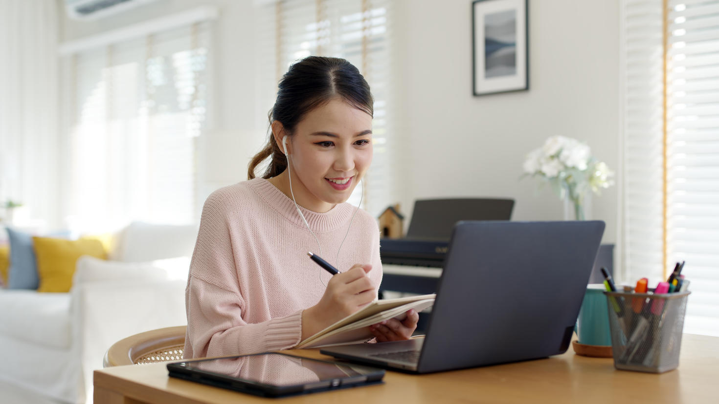 A girl is writing on a notepad and looking at her computer
