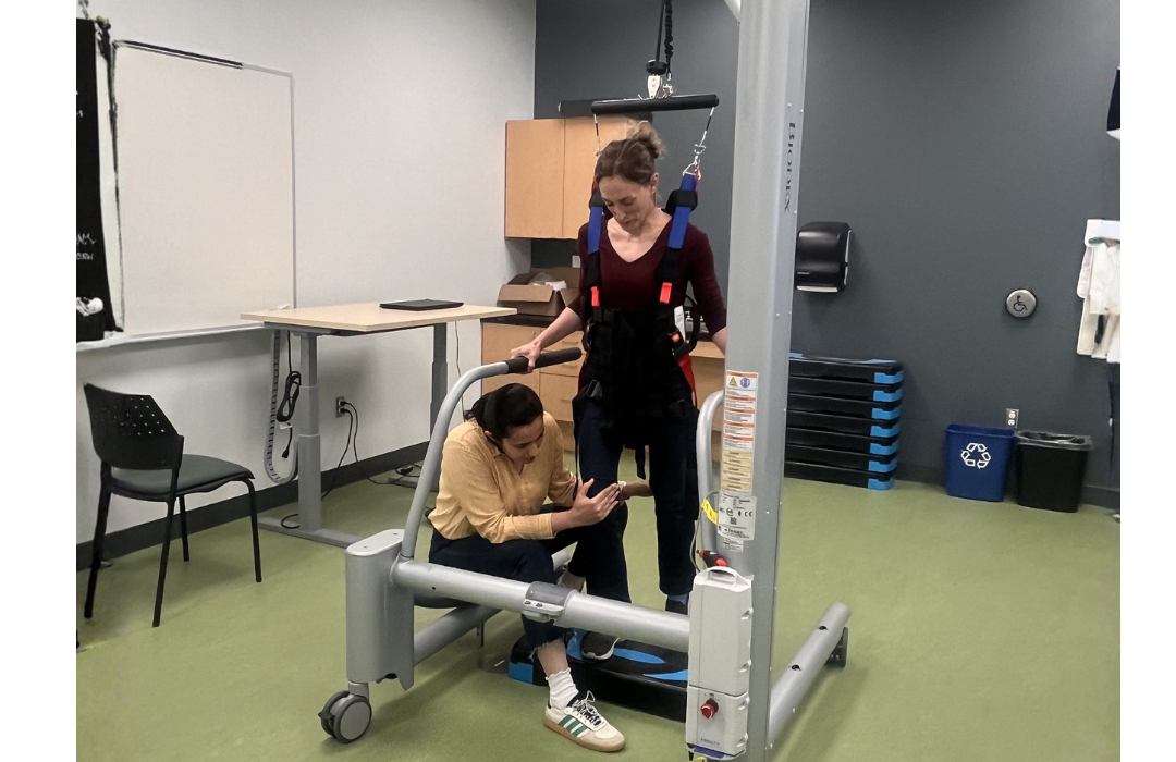 A participant is using specialized laboratory equipment in mobility support under the guidance of a research assistant