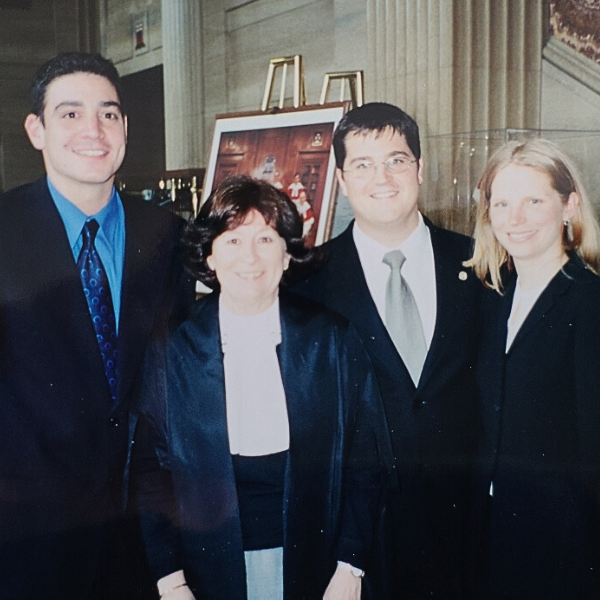 Four people face the camera. Three of them are wearing suits, while one is wearing judges' robes.