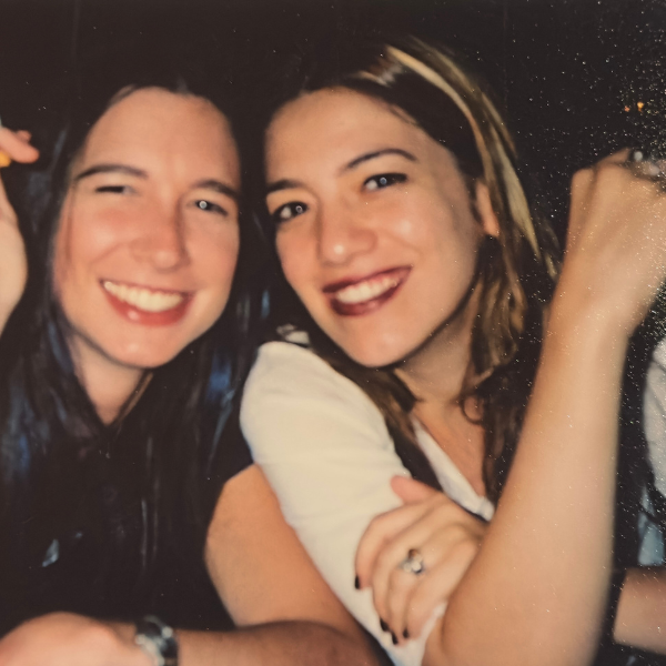 Two young women smile and lean into one another.