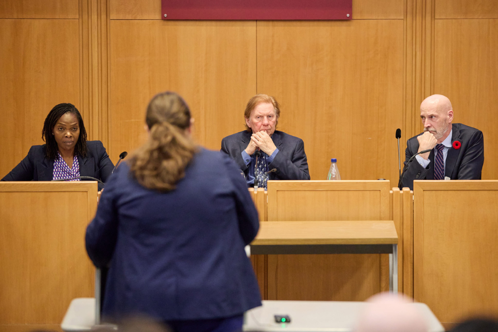 Three judges for the Nelligan Moot Competition sit at bench facing an appellant at the podium.