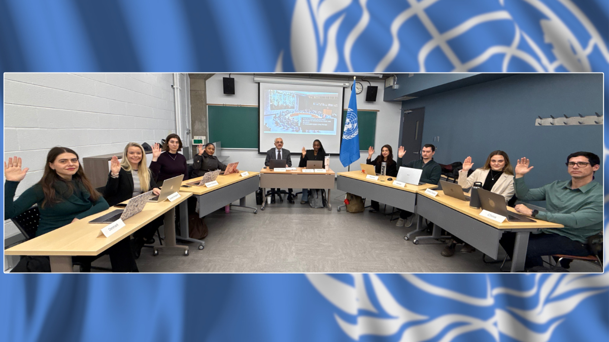 Nine students sit in a classroom and all are raising their right hands