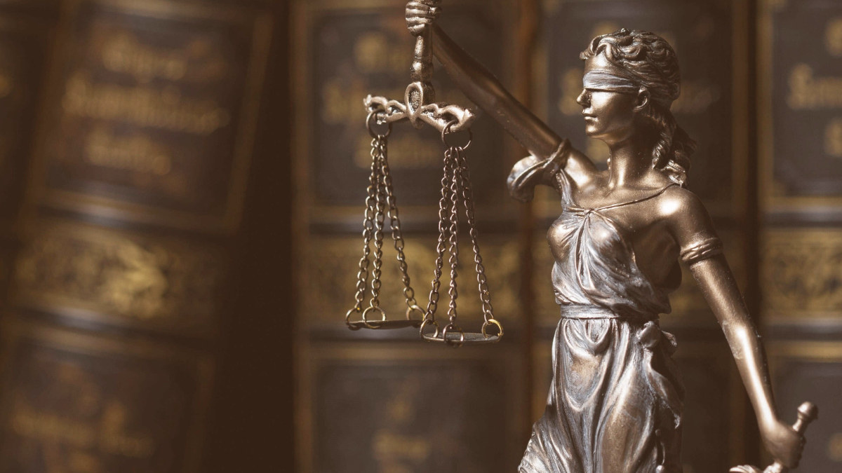 Statue of Lady Justice, holding the scales of justice in one hand and a sword in the other, in front of a shelf of books