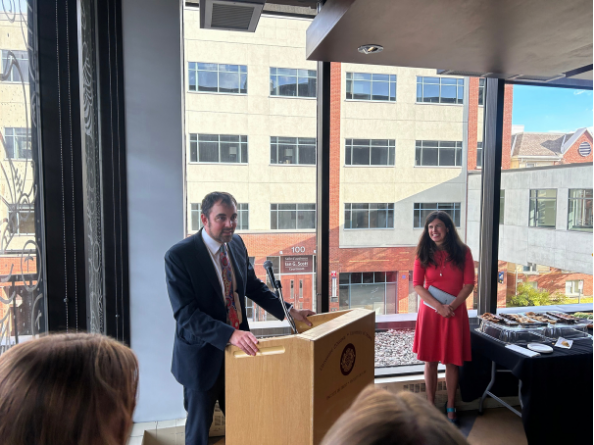 Image of a man behind a podium and a woman on the side watching