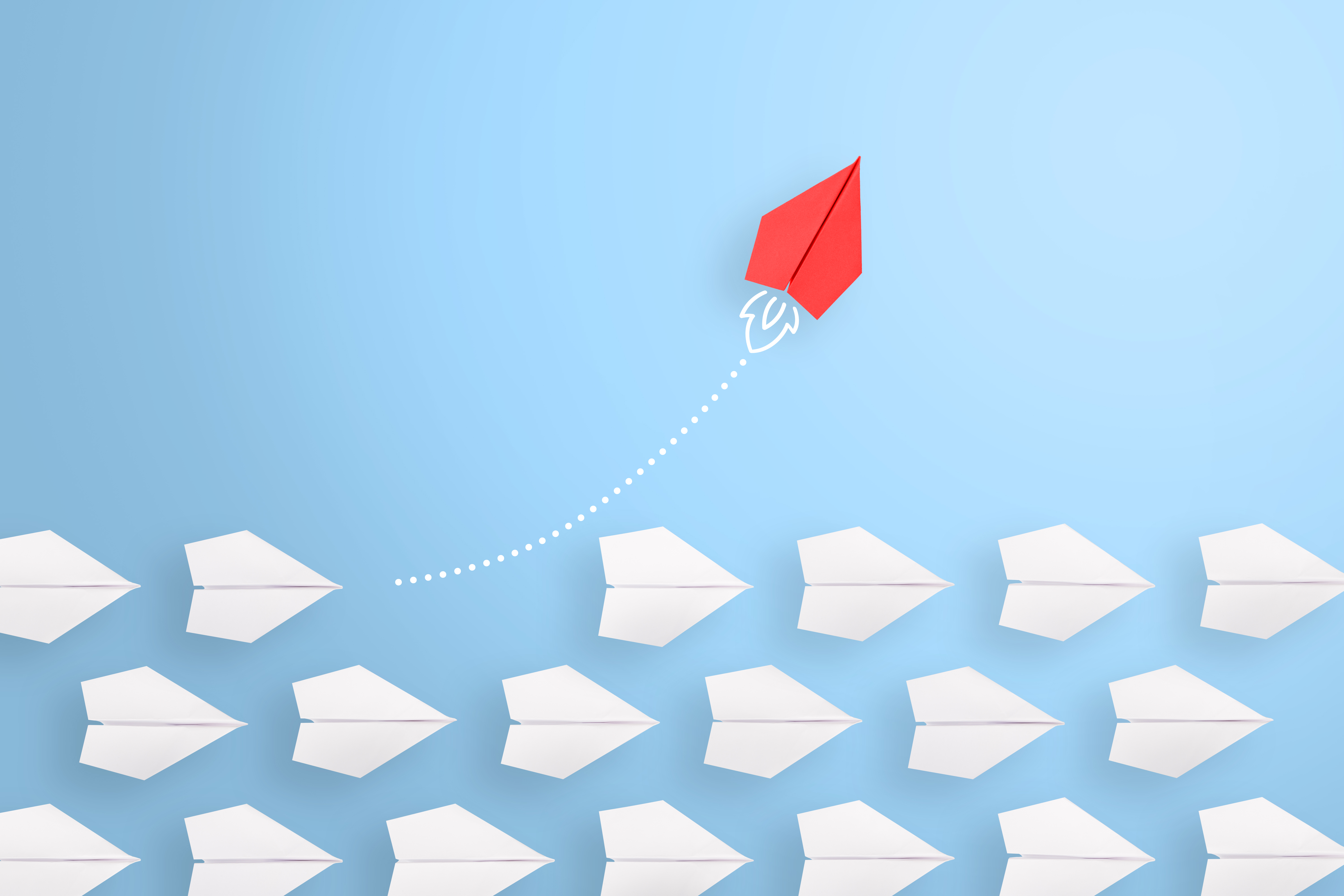 A single red paper airplane rising above rows of white paper airplanes against a light blue background.