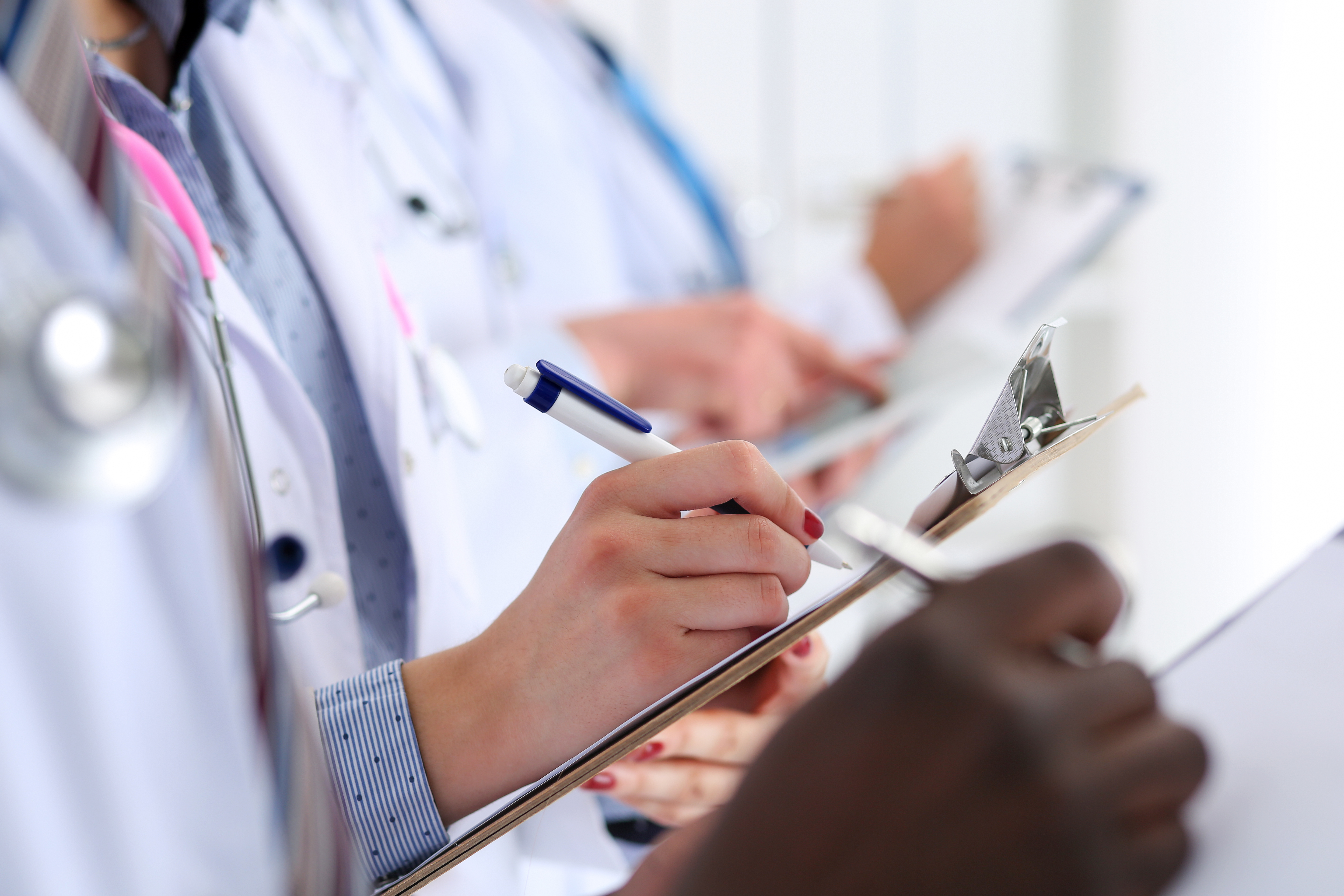 Group of doctors hold pens and clipboard pads make some notes during medical conference