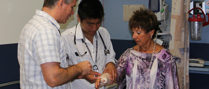 Photograph showing a male resident tending to a patient&#039;s arm with the supervision of his preceptor
