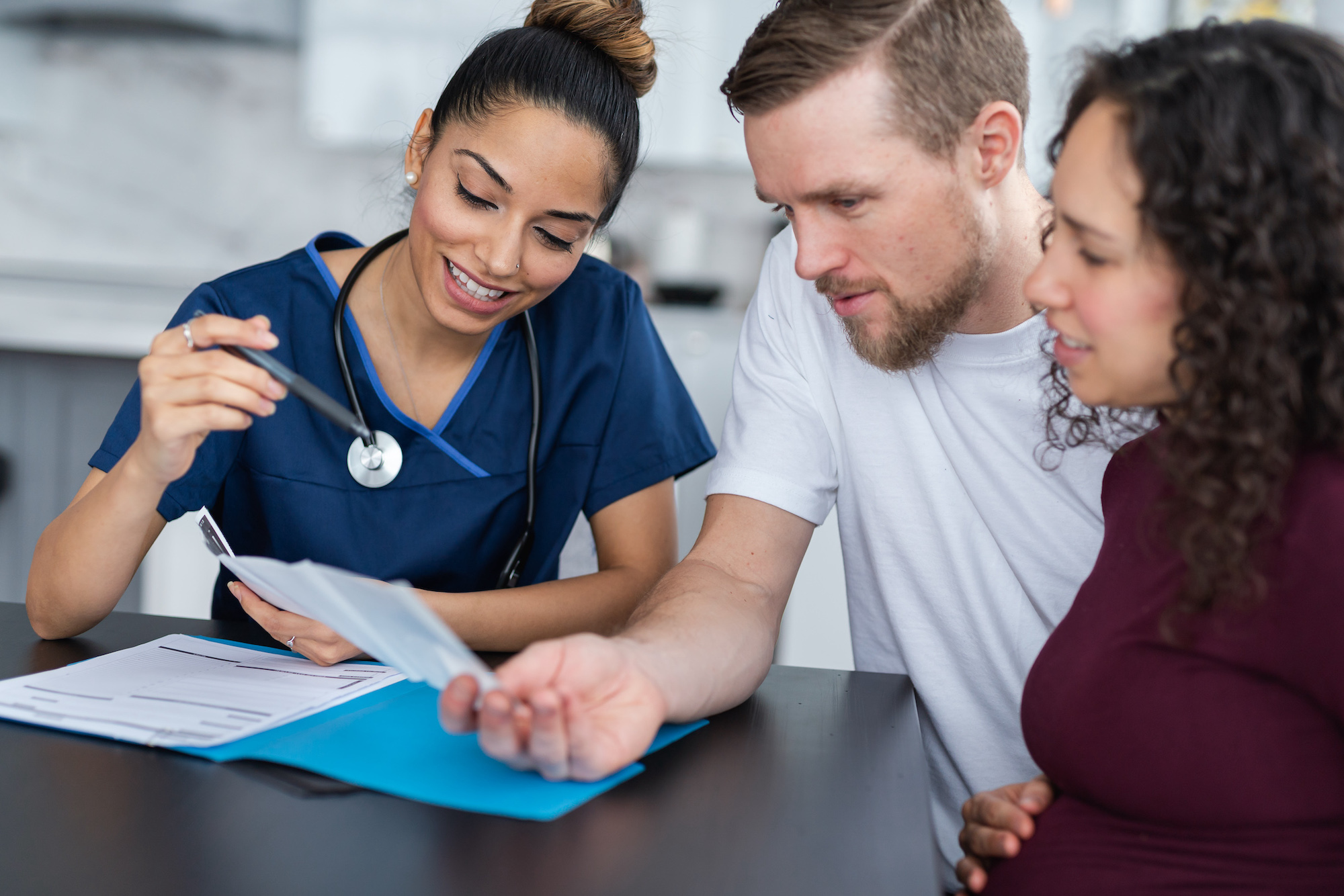 An attractive female doctor is showing an expecting couple their ultrasound sonogram. The couple are excited.