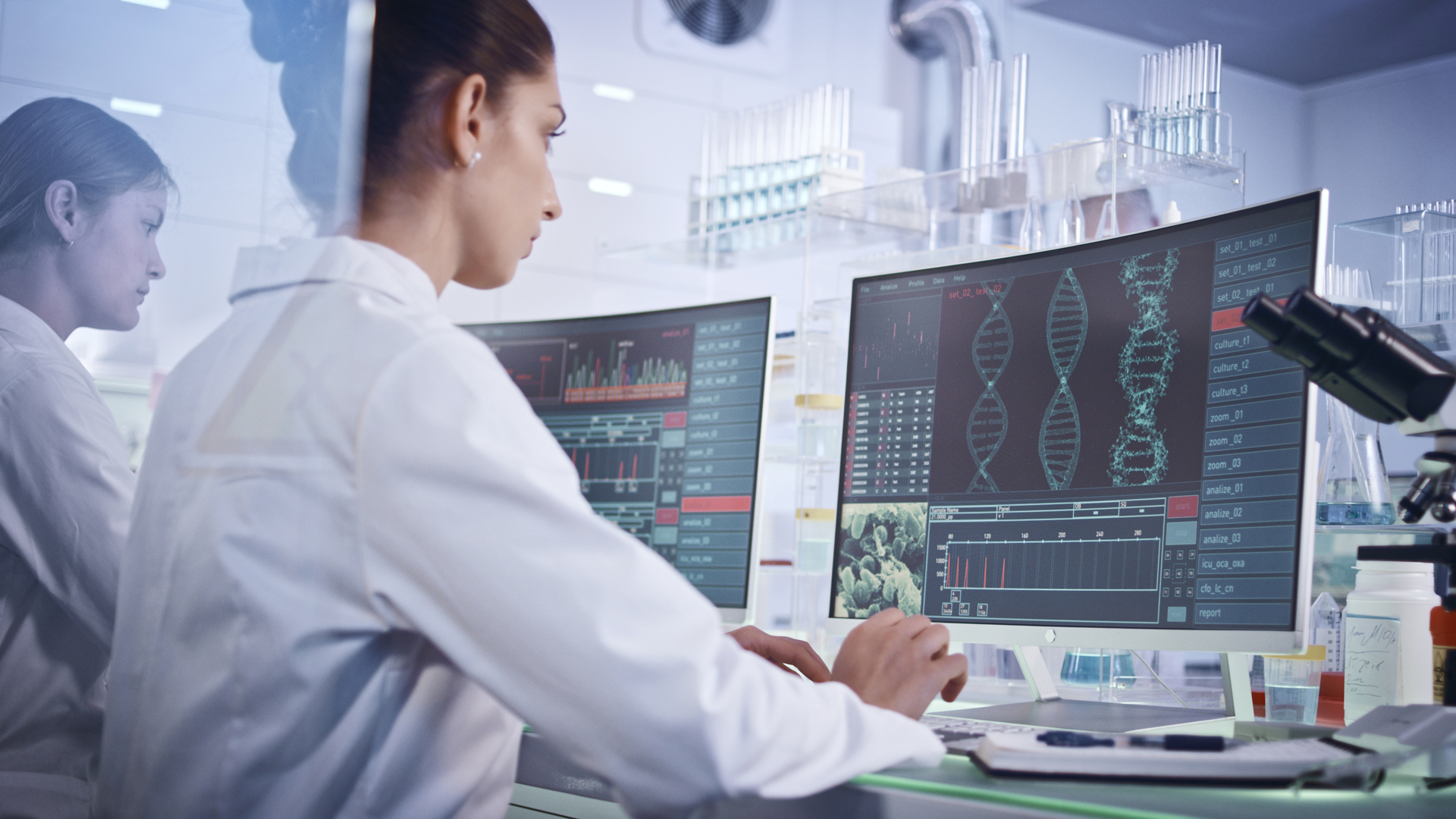 Female research team studying DNA mutations. Computer screens with DNA helix in foreground