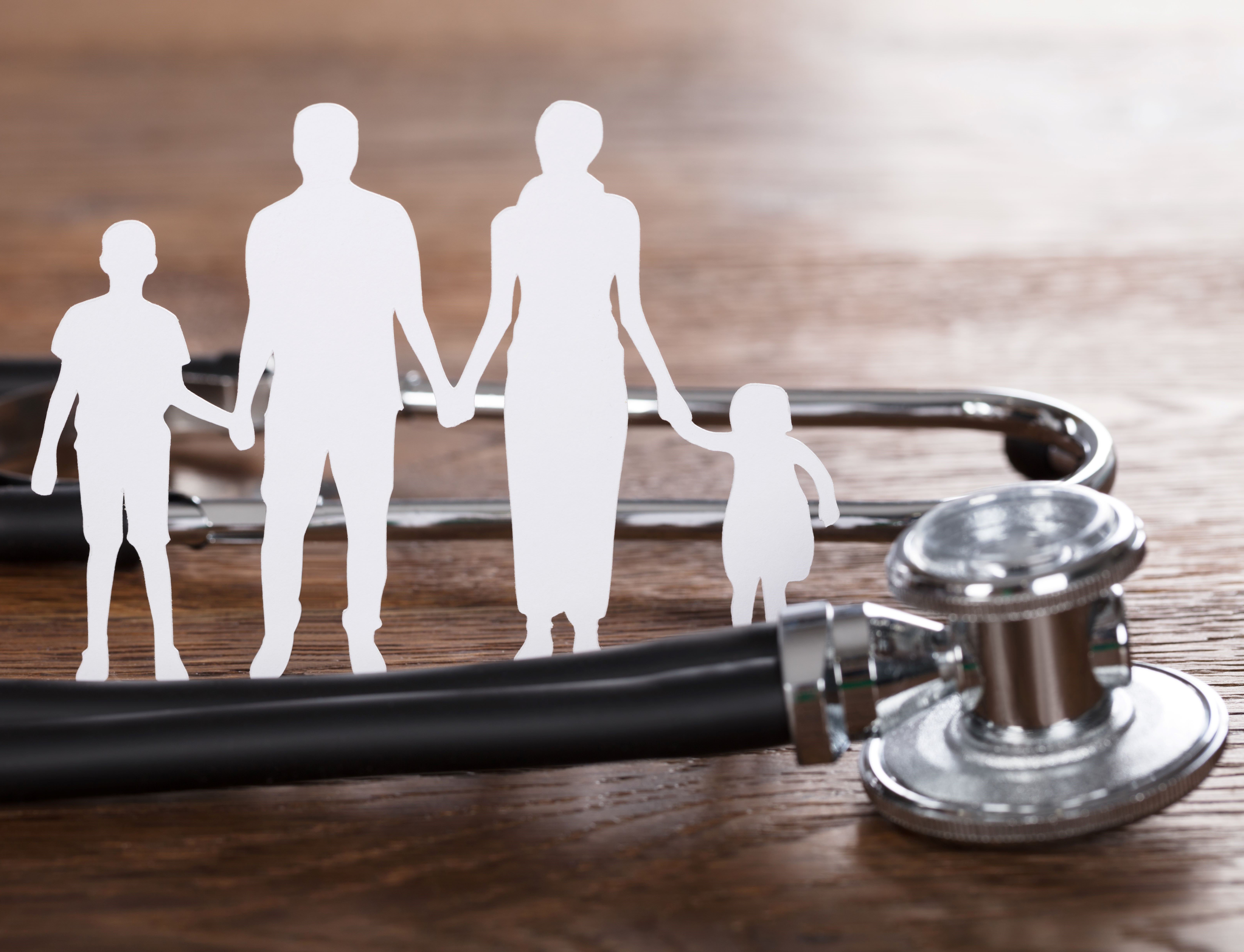 Healthcare concept with a family cut-out and stethoscope at a wooden desk