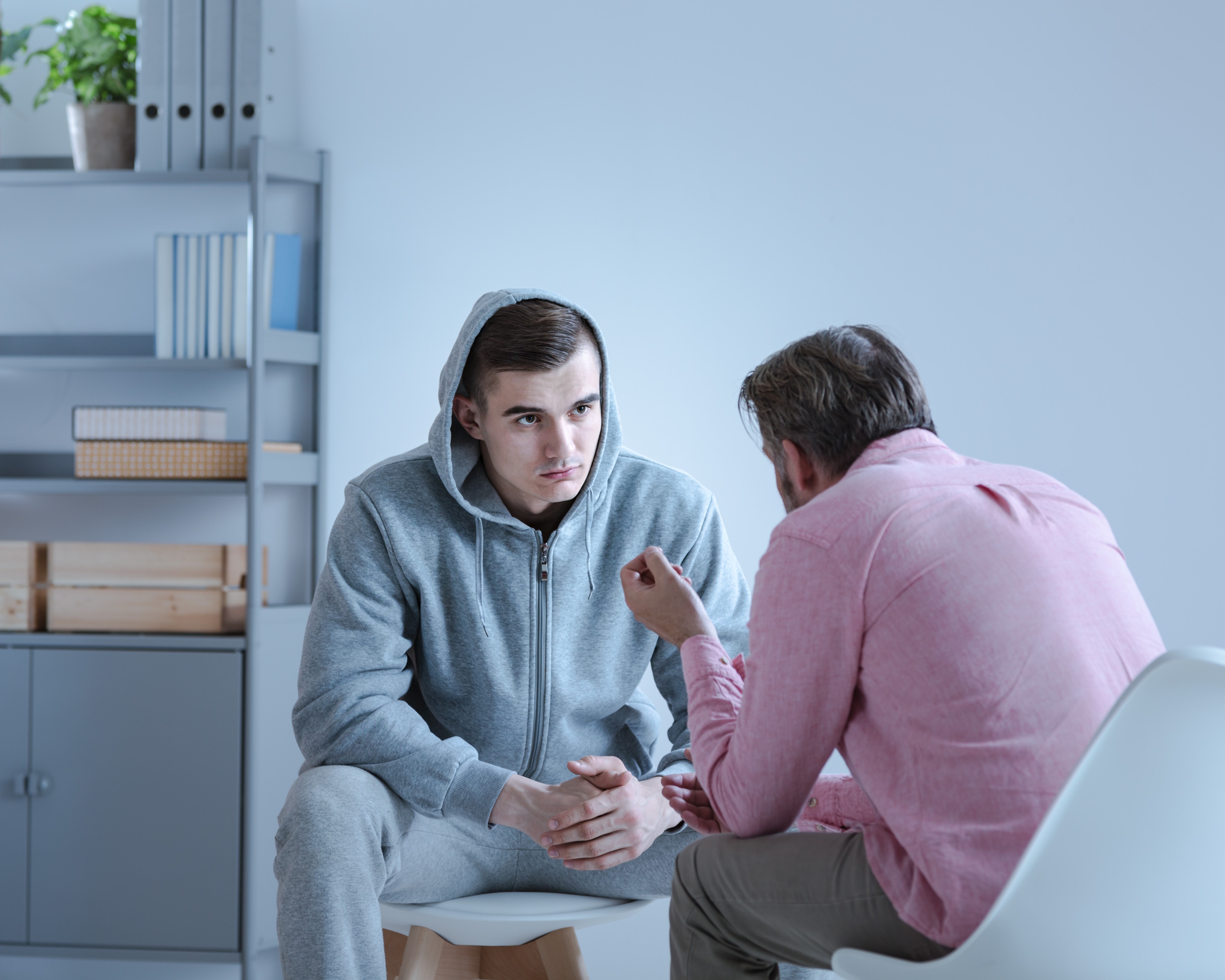 A psychologist explaining an action plan for recovery to a troubled teenage boy during a therapy session.