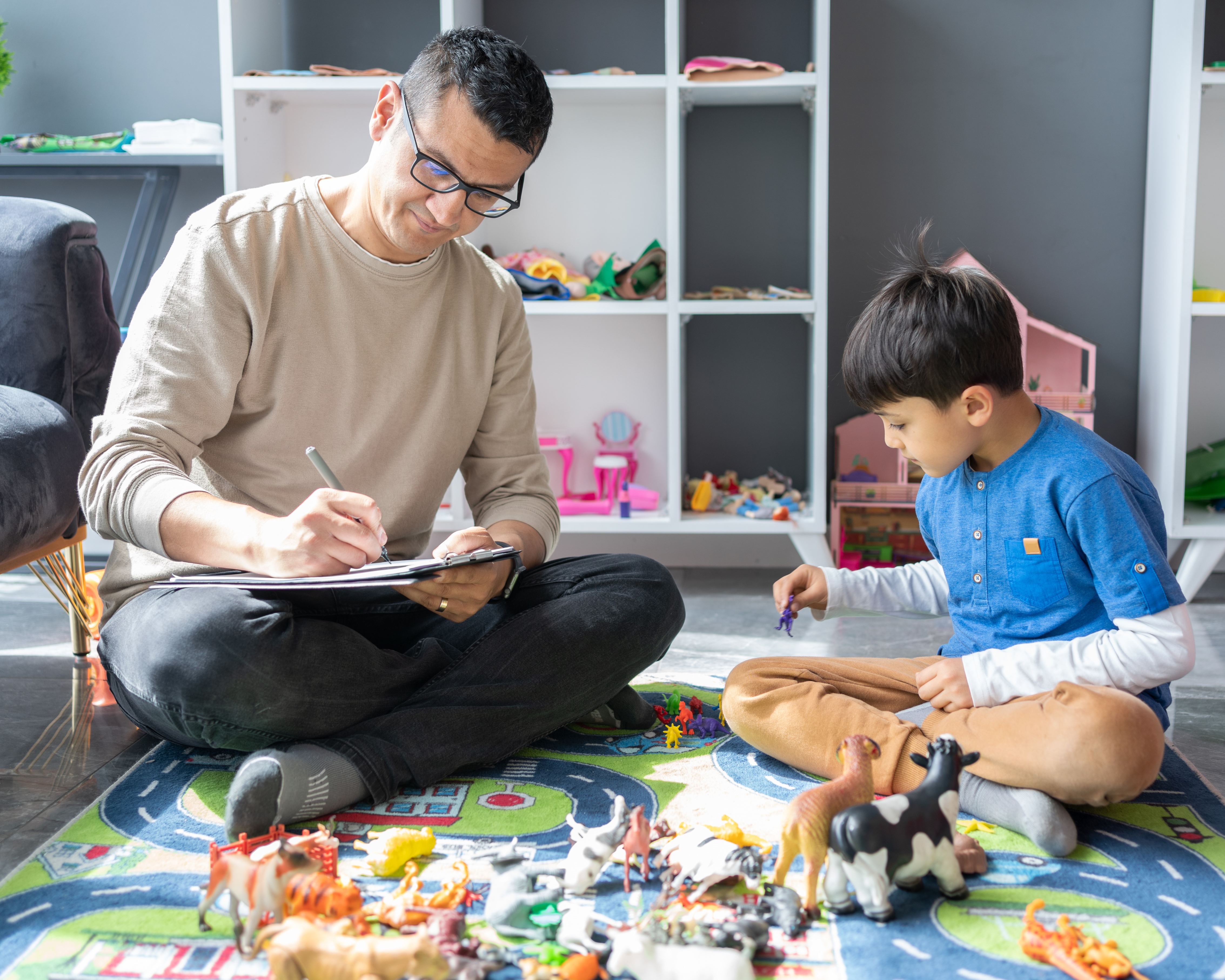 A professional child psychologist observing a little boy playing with toys at a Psychotherapy session