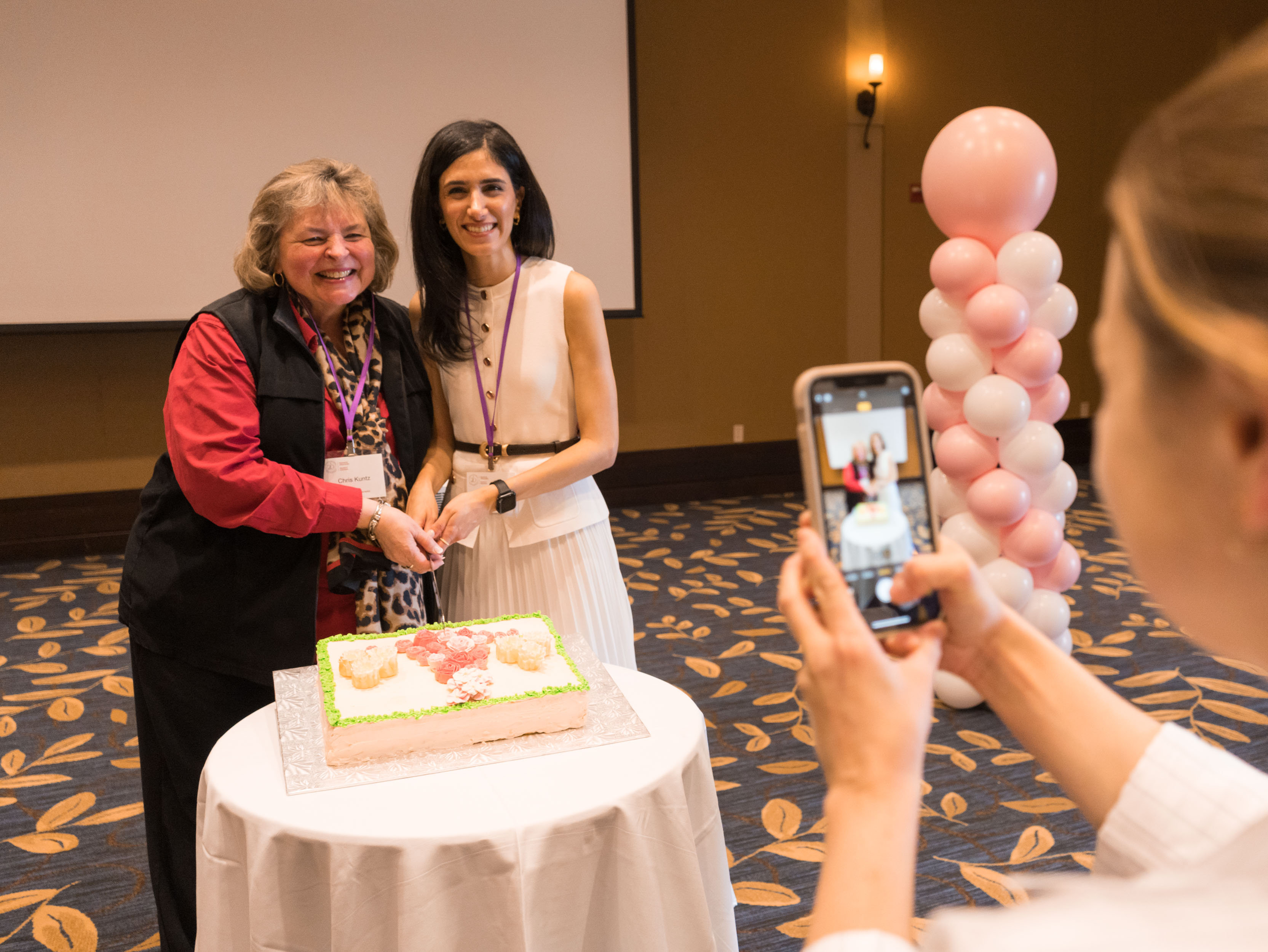Dr. Christiane Kuntz, past program director, and Dr. Elise Azzi, current program director, smile as they cut a ceremonial cake celebrating 20 years of Women’s Health while an attendee takes their photo
