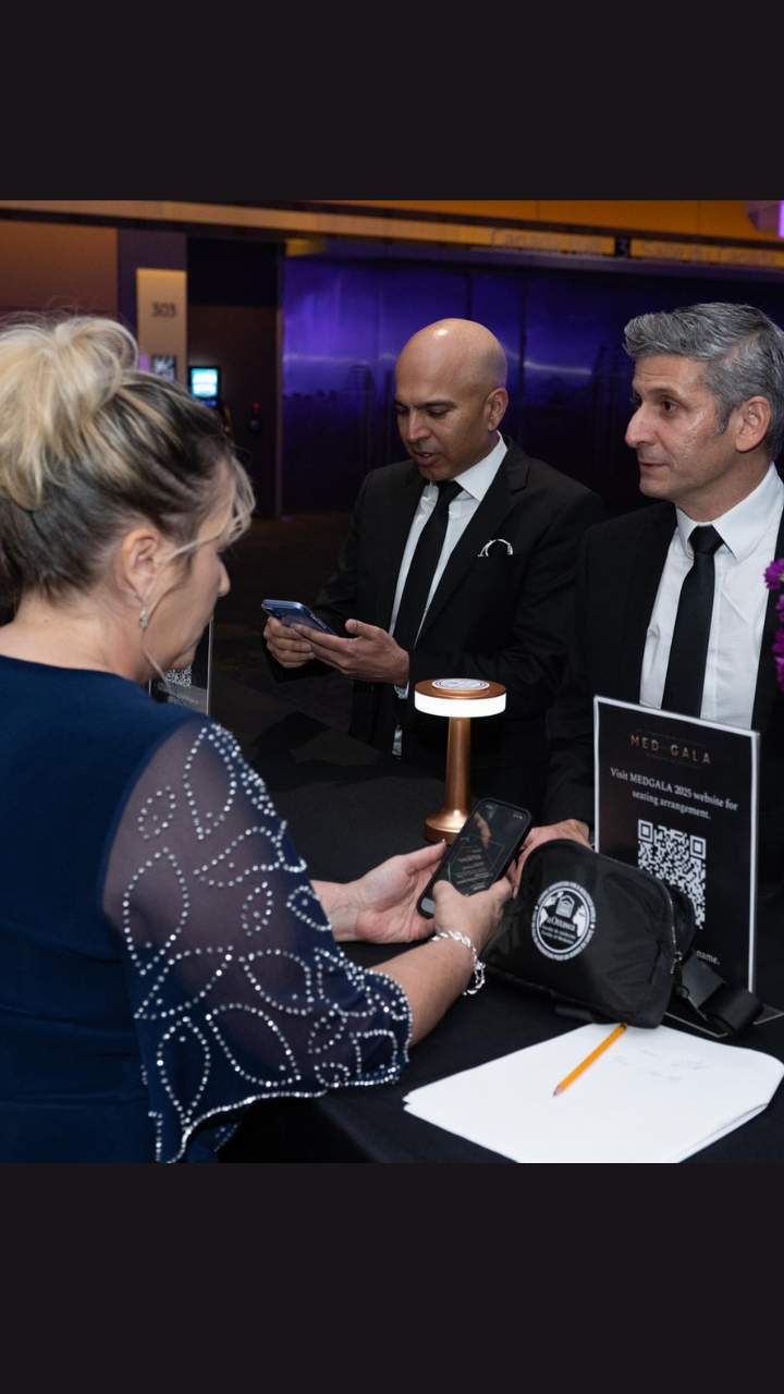  A woman speaks with two men in suits at the MEO Gala booth; one checks his phone beside a QR code.