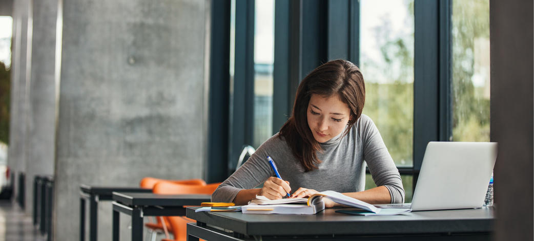 Female caucasian student studying at a desk near a huge window