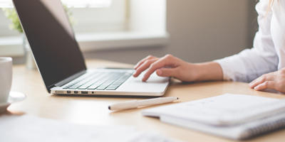 Person typing on a laptop while working at a desk with documents nearby.
