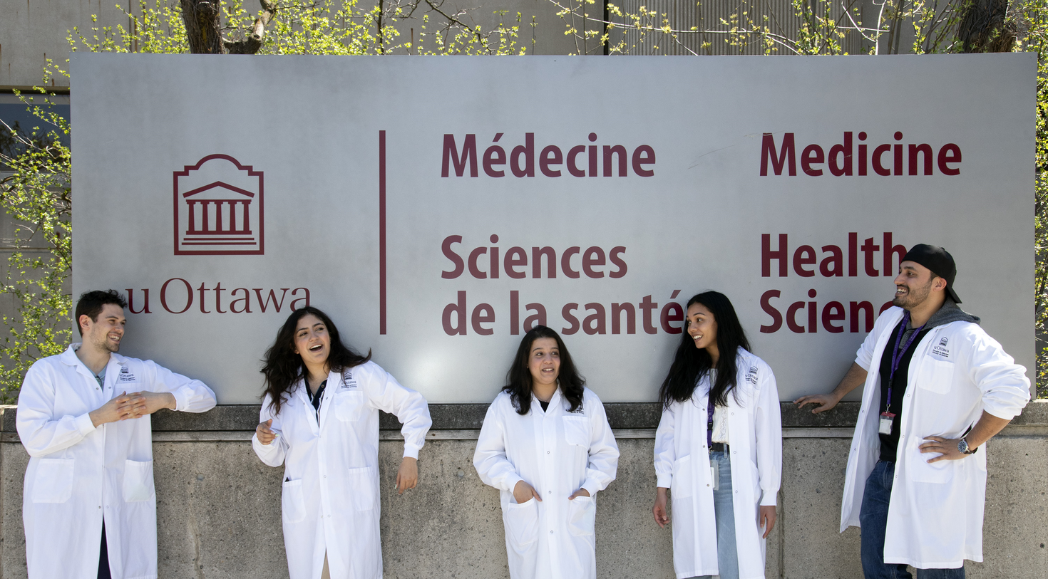 Group of students in lab coat standing in front of Roger Guindon building