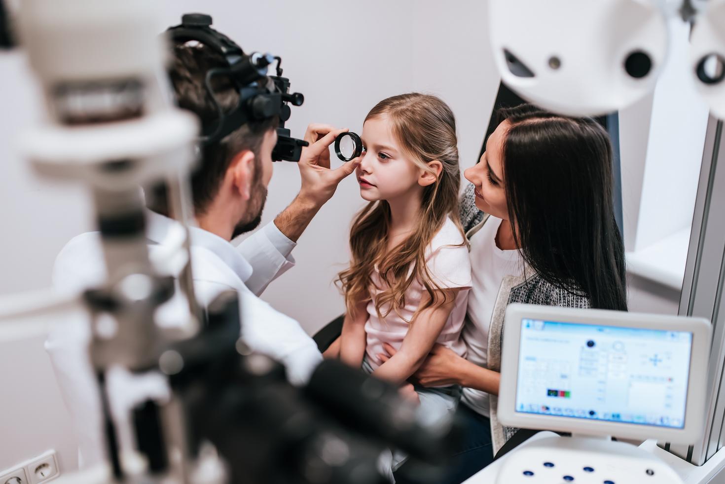 Physician using a lens to examine a child’s eye with a parent present