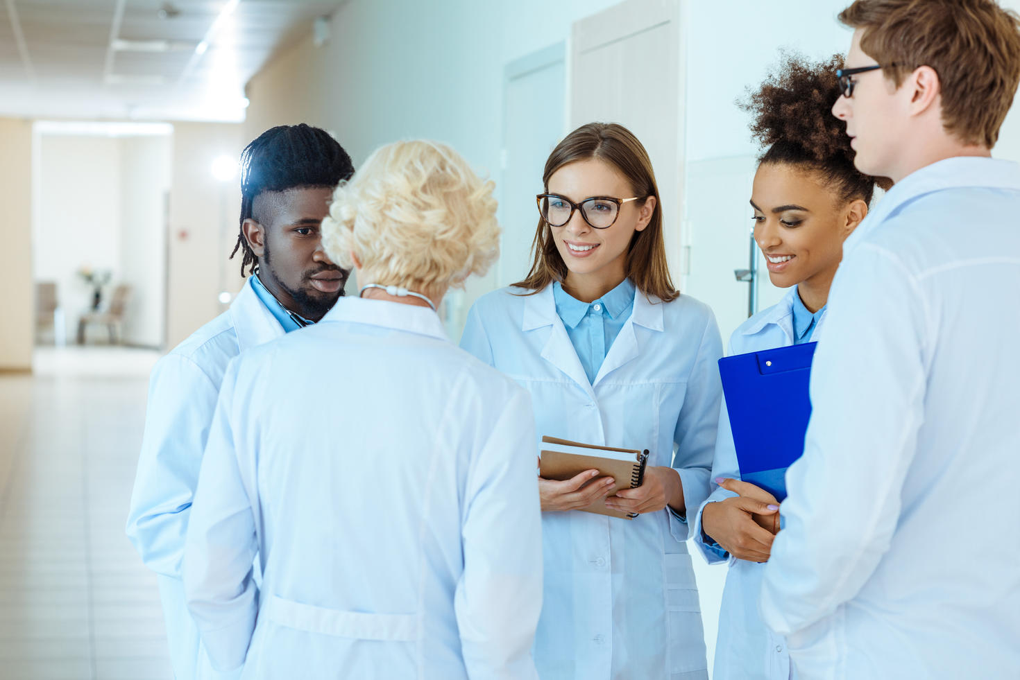 A multiracial group of medical interns in lab coats discussing work with elder doctor
