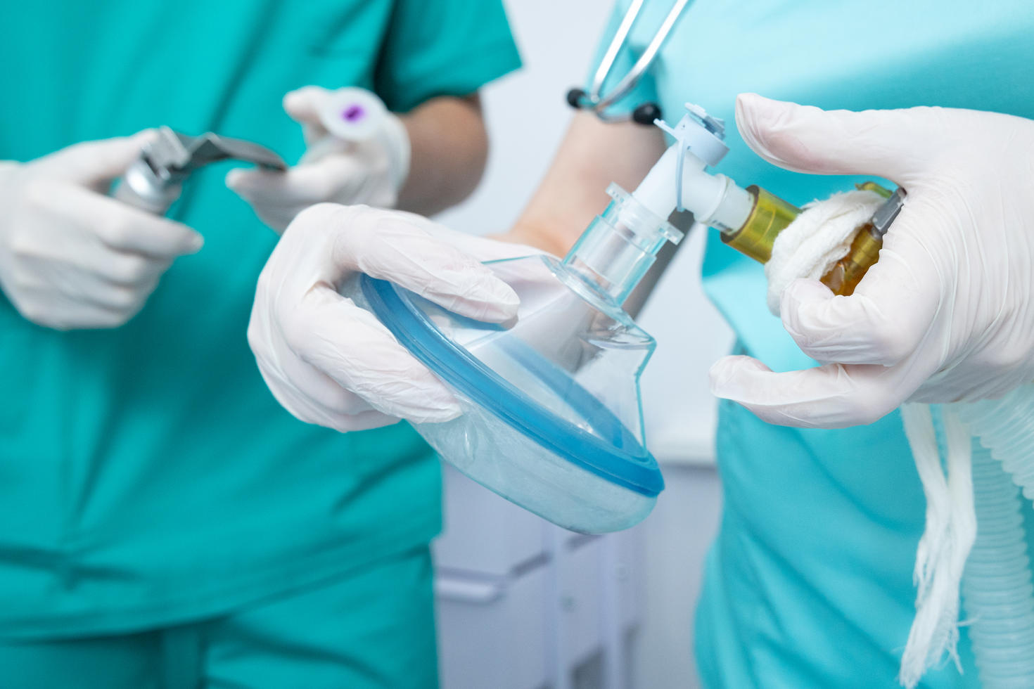 The anesthesiologist holds an oxygen mask in the operating room. The assistant anesthesiologist holds the laryngoscope for intubation of the patient's trachea.