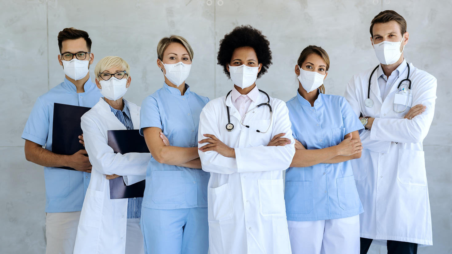 Group of healthcare workers wearing protective face masks while standing with arms crossed and looking at camera.