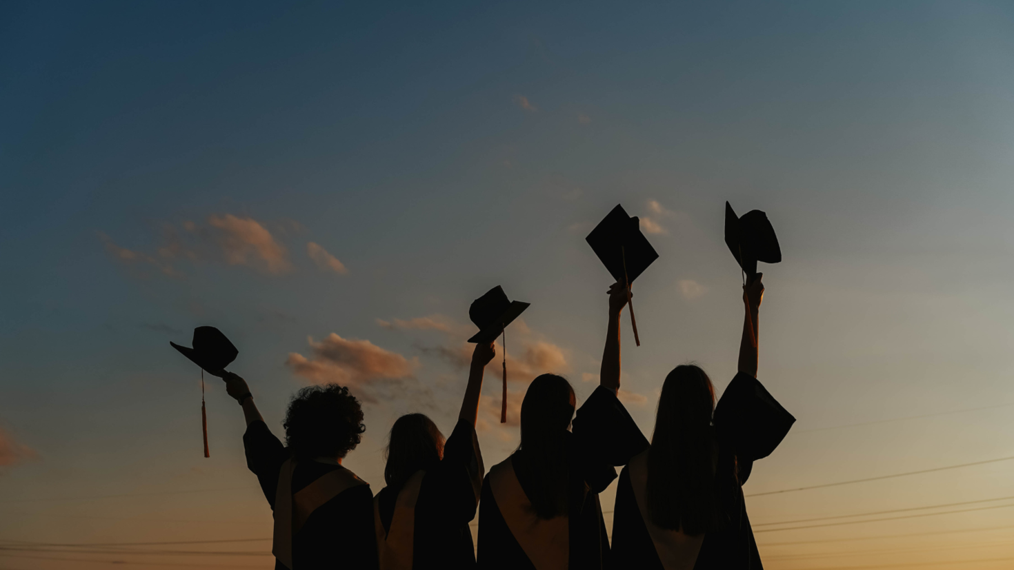 students in silhouette against a sunset in graduation attire